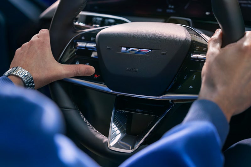 Close-up of a Man About to Press the V-Button on the 2026 OPTIQ-V Steering Wheel | Carlisle Cadillac in Carlisle PA